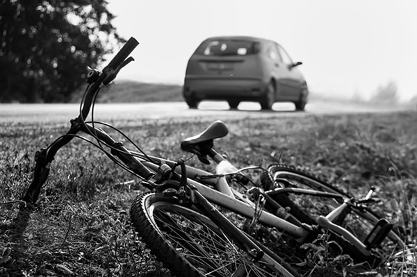 bike laying on grassy side of road with car driving away