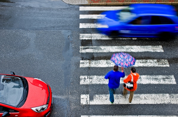 Couple walking in crosswalk with umbrella and cars driving past them
