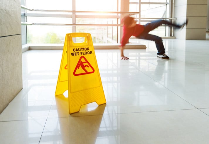 man slipping and falling near caution wet floor sign