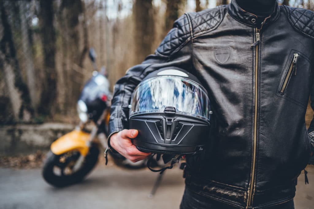 motorcyclist holding helmet with a motorcycle behind