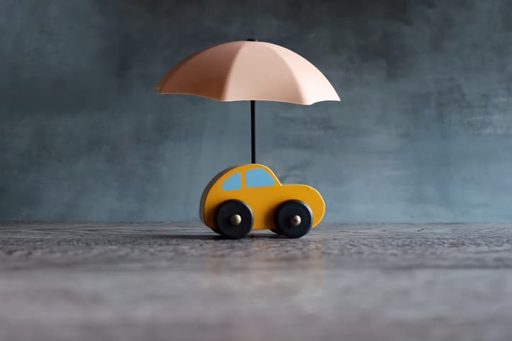 Toy wooden car with umbrella signifying car insurance