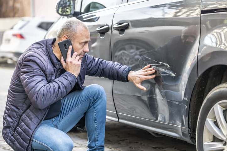 Man on cell phone looking at damage to car 