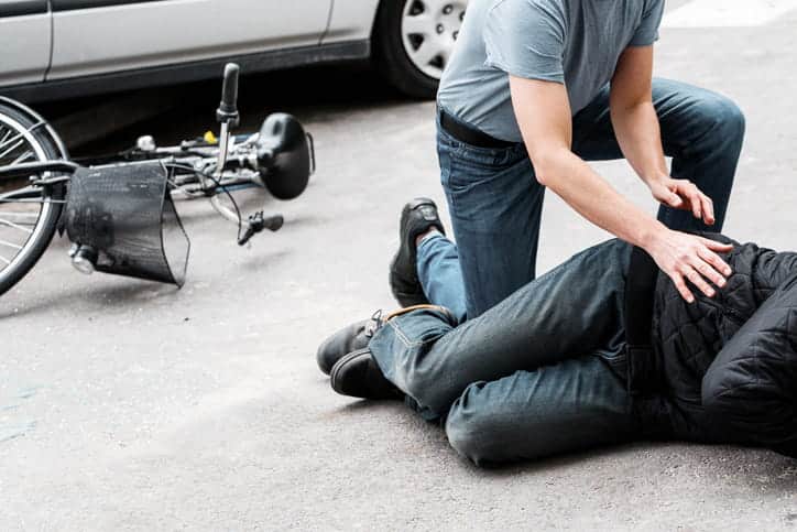 Pedestrian helping a victim of an automobile accident lying on the street next to a broken bike.