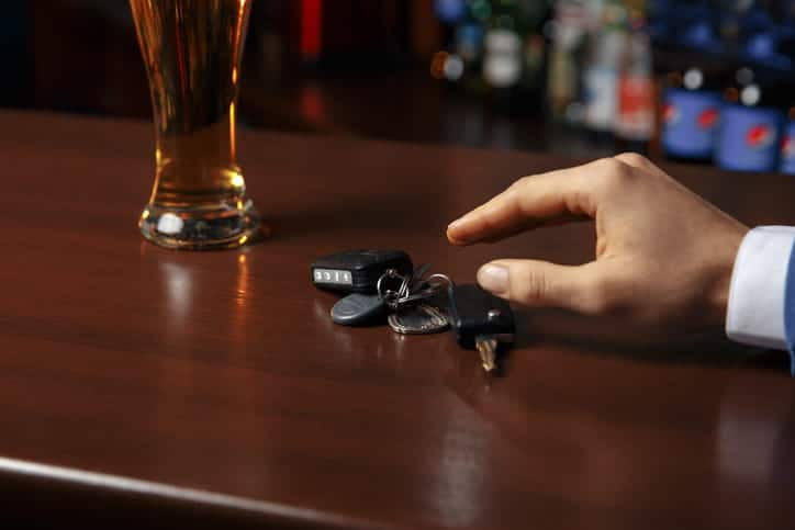 focus is on a hand reaching for car keys that are sitting next to a glass of beer on a bar.