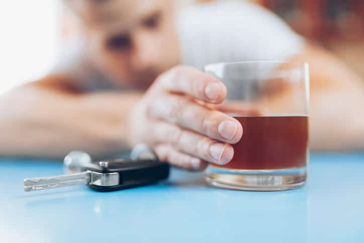 focus is on a set of car keys next to an alcoholic beverage. A man holding the glass is blurred out in the background.
