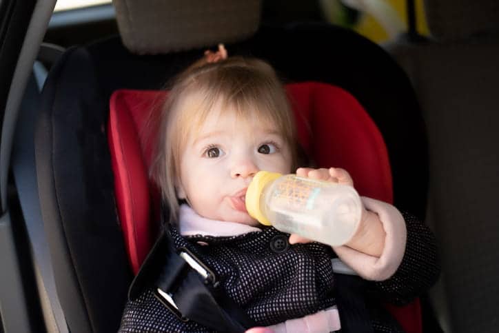 A child drinking her water while in a car seat.