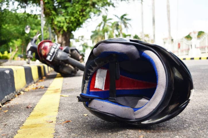 An image of a motorcycle helmet on the ground, with the bike crashed in the distance. The victim filed an injury claim from a motorcycle crash afterwards.