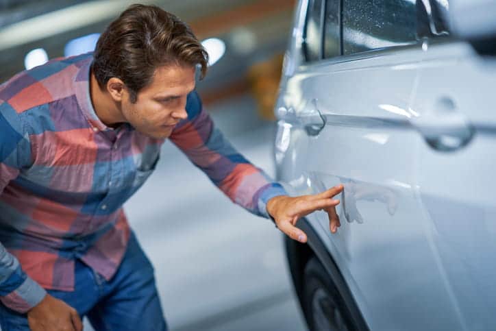 A man inspects his parked car after it's been hit.