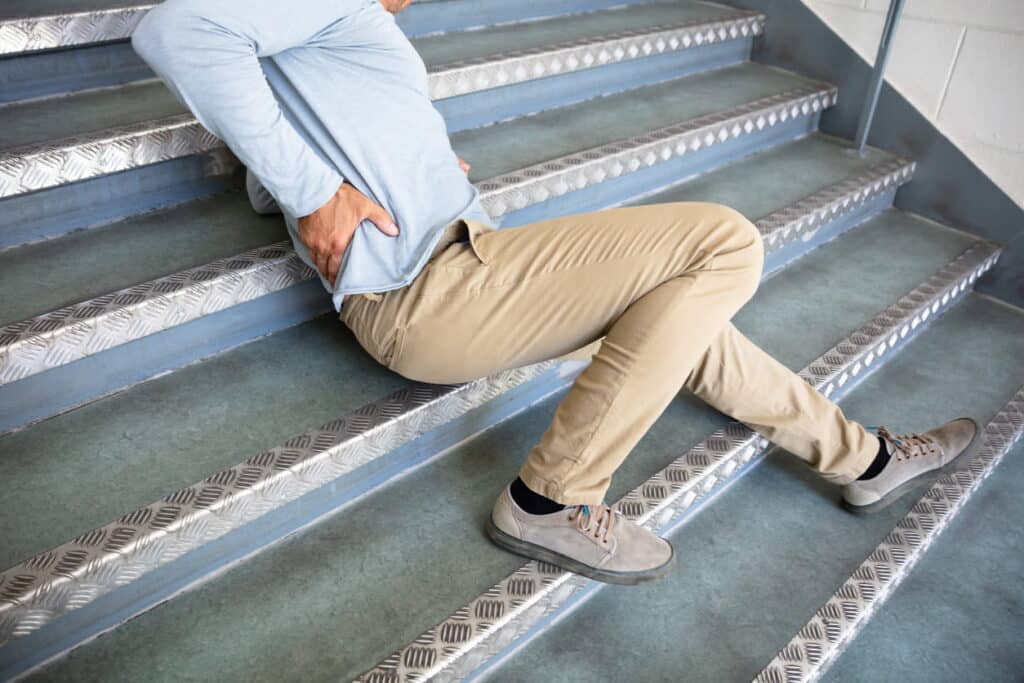 A man sitting on the stairs, holding his back, after a slip and fall accident.
