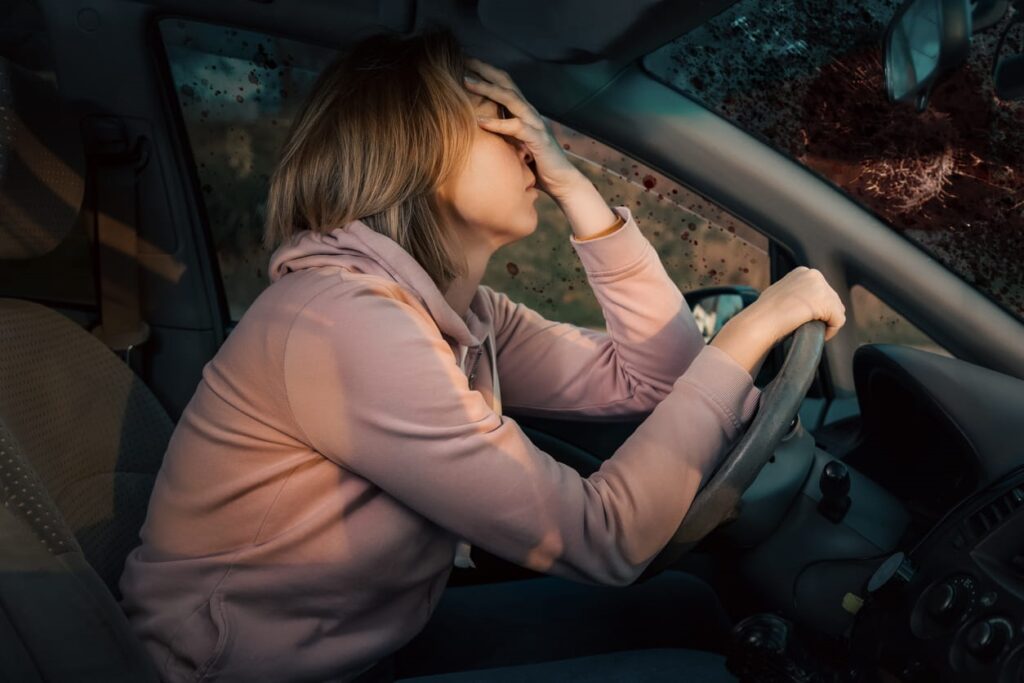 A woman holding her face with one hand, the other is on the steering wheel after drunk driving.