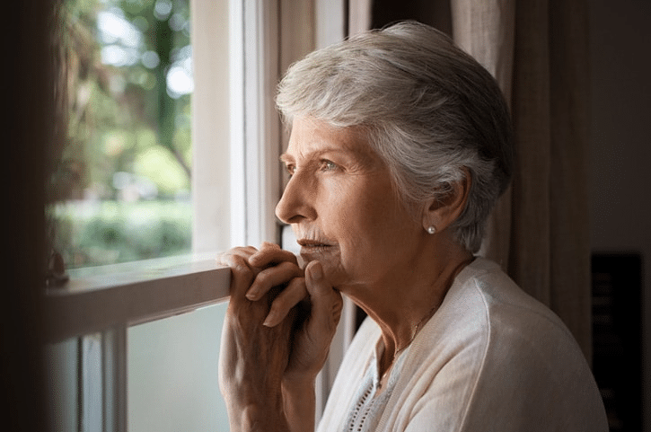 An elderly woman sitting at a window staring outside