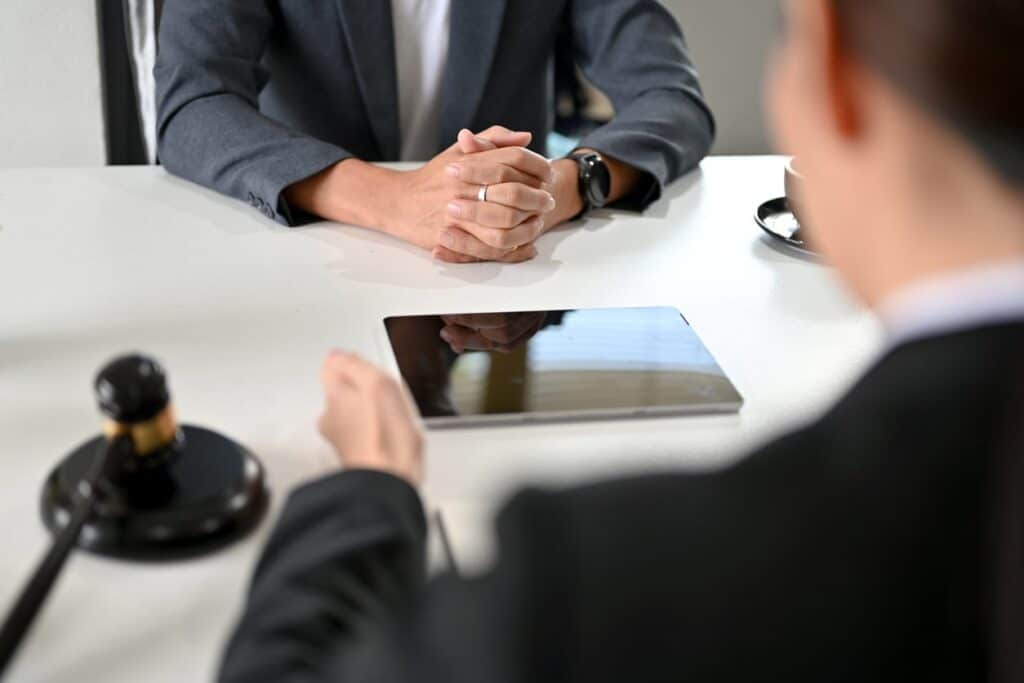 Closeup of a personal injury lawyer speaking with their client. On the desk between them is a tablet and a gavel.