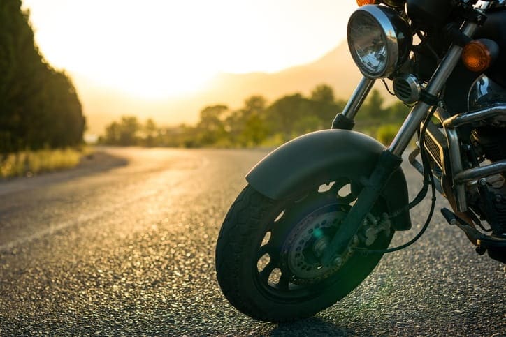 The front tire of a motorcycle parked on the road during dusk. 