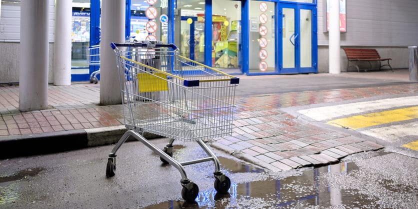 A grocery cart outside of a grocery store near a puddle. 