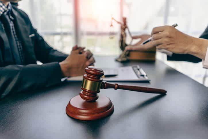 A Tampa Wrongful Death Attorney Is Discussing A Case With Their Client. In Front Of Them Is Paperwork, A Gavel, And A Lady Justice Statue In The Background.