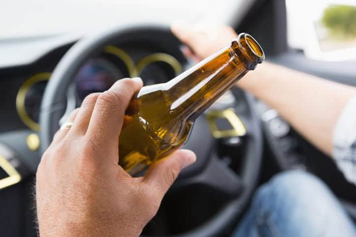 A drunk driver holding a beer behind the wheel of a car