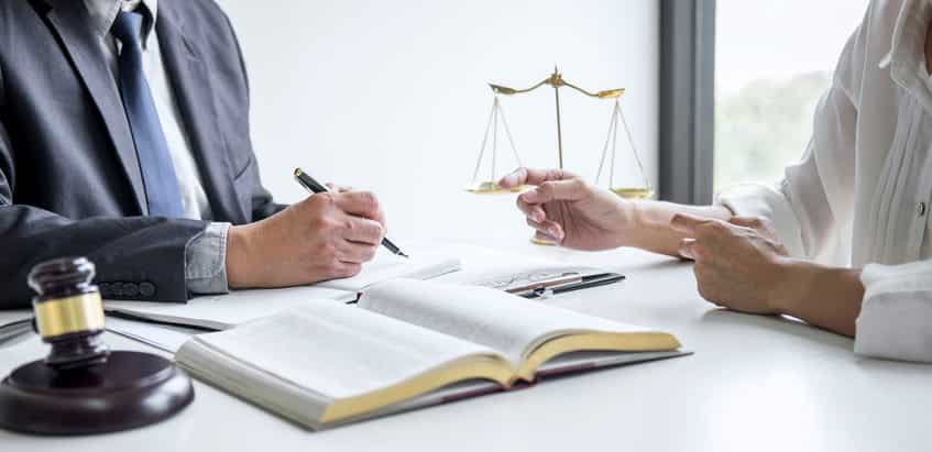 A Brandon, Florida, car accident lawyer is reviewing paperwork with their client. In front of them is a gavel, an open book and the scales of justice. 