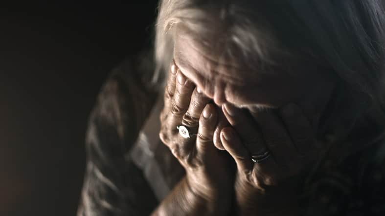 An Elderly Woman Holding Her Head In Her Hands Sadly.