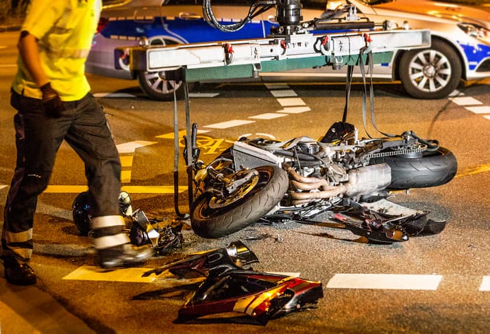 A Tow Truck Driver Lifting A Wrecked Motorcycle Off Of The Road
