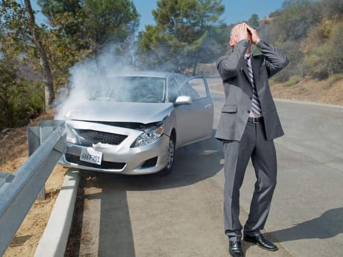 A Car Crashed Into A Guard Rail. The Driver Is Holding His Face In Anguish