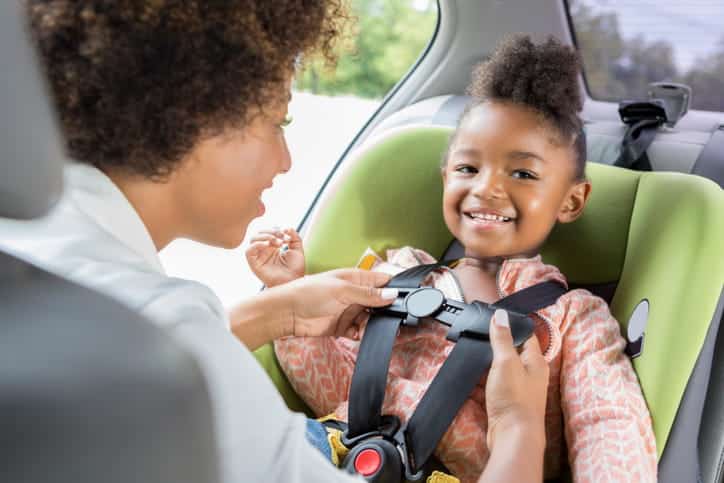 A woman strapping her young child into a car seat. 