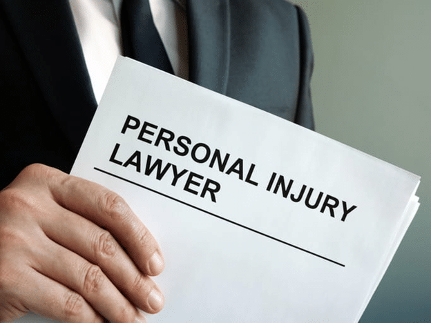 A Hand Holding A Document Titled &Quot;Personal Injury Lawyer&Quot; With A Person In A Suit In The Background.