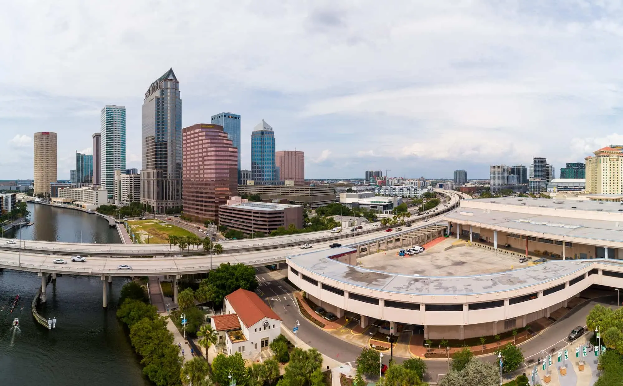Jack Bernstein, Injury Attorneys 4 Aerial Panoramic View Of Downtown Tampa, Florida, Showcasing The City Skyline With High-Rise Buildings Along The Hillsborough River, Elevated Highways, And Palm Tree-Lined Streets Under A Cloudy Sky.